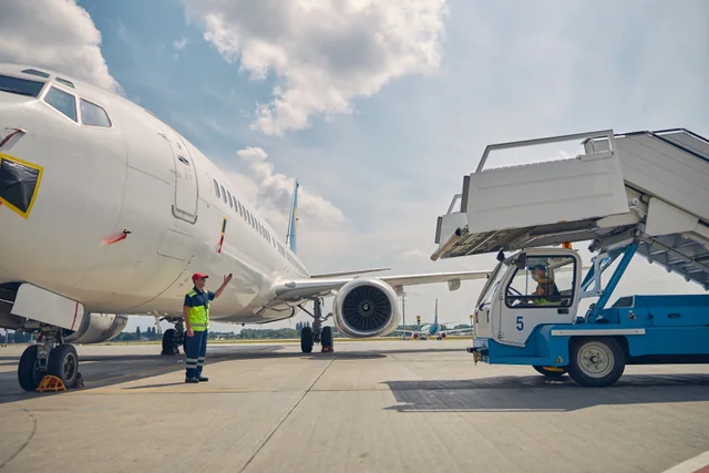 Personal de tierra y escaleras de embarque junto a un avión de pasajeros. Imagen ilustrativa; no muestra este aeropuerto.